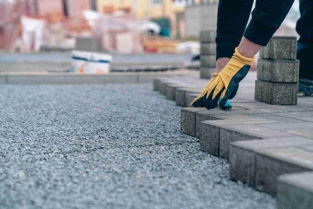 Worker placing concrete pavers on a gravel base for professional driveway installation