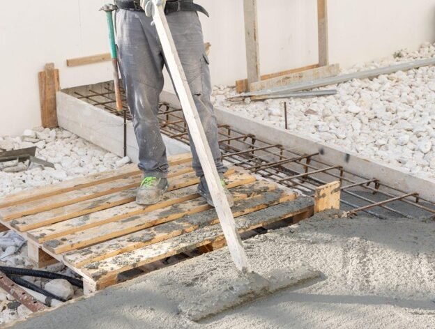 Contractor leveling freshly poured concrete with screed during patio construction process
