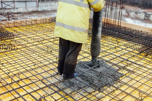 Concrete contractor pouring wet concrete into a reinforced rebar grid for slab foundation installation