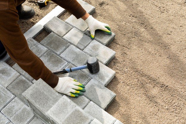 Contractor installing concrete pavers with a rubber mallet during the driveway installation process