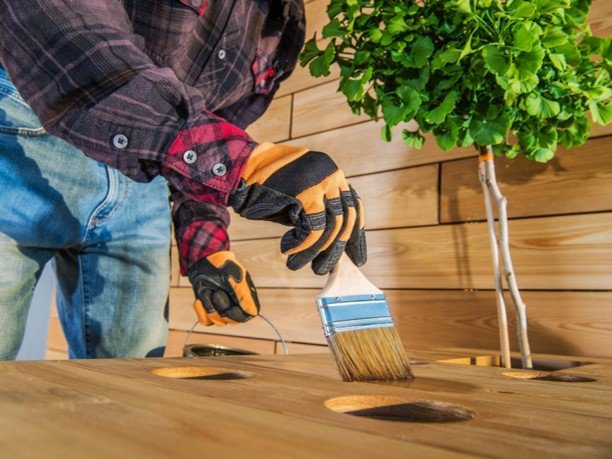 A professional painting brown deck using paint brush.