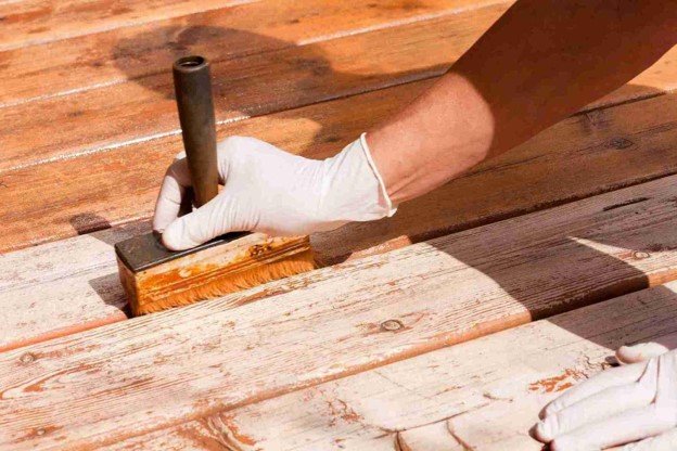 A man working on refinishing deck with a gloves on it.