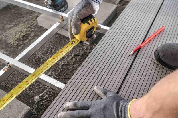 A professional working composite deck installation while there is pen and holding ruler tape.