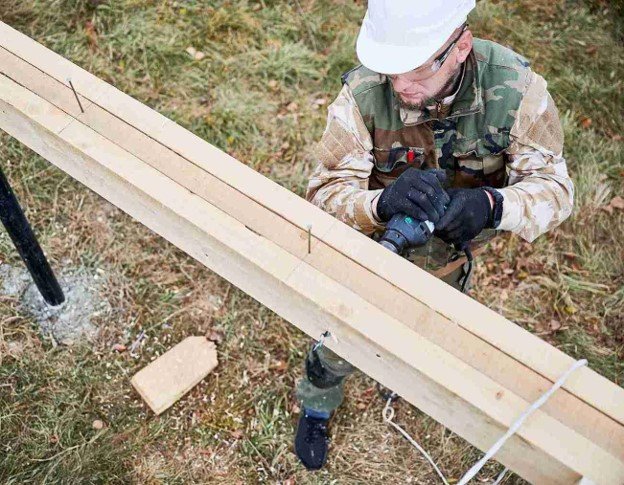Man drilling on wood while building on fence.