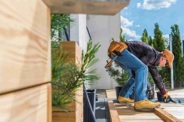 A worker refinishing deck with tool on the side