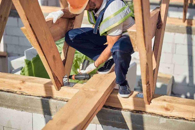 A man drilling on wood while on the top working on pergola construction.