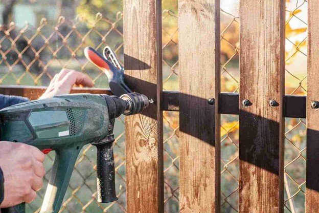 A man working on fence while drilling on it.